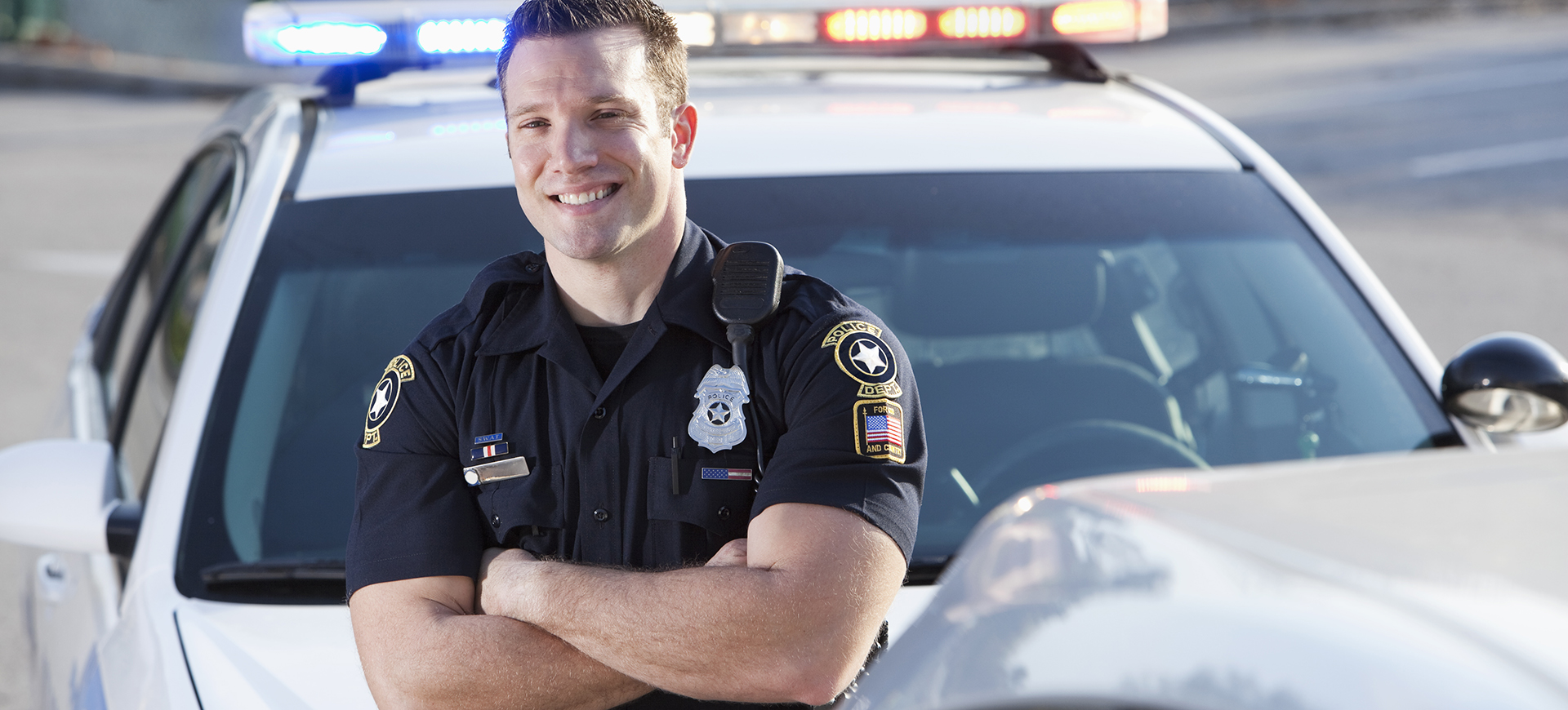 Police officer (20s) standing in front of cruiser.