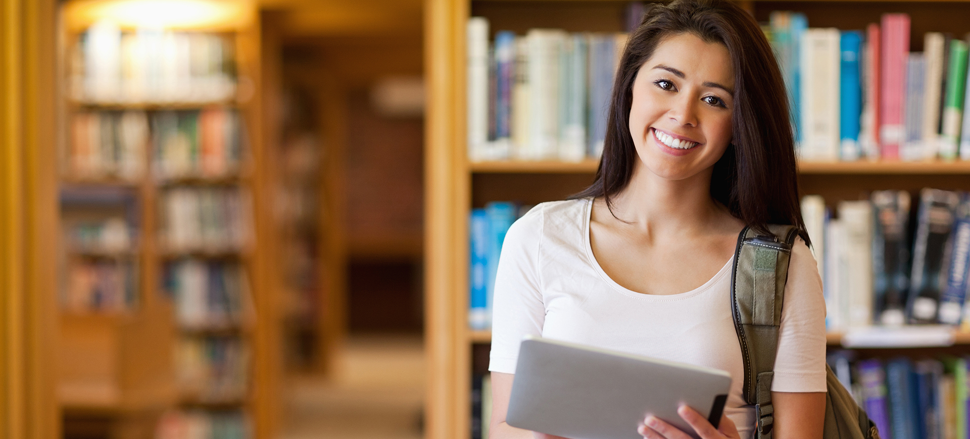 Smiling student using a tablet computer in a library